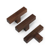 Trois boutons Vigio en noyer de yessential.fr en brun foncé sur fond blanc. Les boutons en bois en forme de T sont placés à différents angles pour mettre en valeur le design élégant et la qualité de l'artisanat.