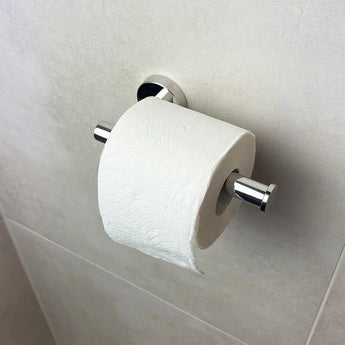 Un rouleau de papier toilette blanc est suspendu à l'élégant porte-rouleau de papier toilette Tino Chrome de yessential.fr contre un mur de salle de bain légèrement carrelé et ajoute une touche moderne à vos accessoires de salle de bain.