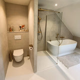 Salle de bain moderne avec toilettes suspendues, luminaires dorés, douche à l'italienne et far et bain autoportant. Le porte-brosse de toilette Branco Gold de yessential.fr repose sur la combinaison de toilettes et l'intégration d'un décor minimaliste.