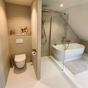 Salle de bain moderne avec toilettes suspendues, luminaires dorés, douche à l'italienne et far et bain autoportant. Le porte-brosse de toilette Branco Gold de yessential.fr repose sur la combinaison de toilettes et l'intégration d'un décor minimaliste.