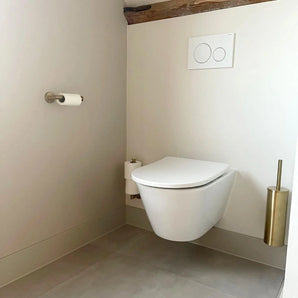 Salle de bain minimaliste avec toilettes suspendues et ensemble de toilettes à double chasse Corrado Gold de yessential.fr, porte-brosse de toilette doré, porte-papier peint et rouleau de rechange. Design élégant dans des tons neutres.