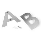 Deux lettres métalliques, A et B, sont représentées sur une surface blanche. Le A est fourni avec le matériel de montage, tandis que le matériel de montage supplémentaire et les chevilles murales à proximité facilitent l'installation - idéal pour les élégants numéros de maison yessential.fr Adamo en acier inoxydable de 15 cm.