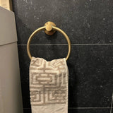 Une serviette au motif beige suspendue au-dessus de l'Elarbo Gold de yessential.fr, un élégant anneau porte-serviettes fixé au mur de la baignoire et une pierre sombre.