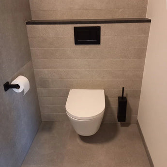 Une salle de bain moderne avec des toilettes suspendues, du carrelage gris, un bouton de chasse d'eau noir, la brosse WC noir mat yessential.fr Alessino Black avec support et un porte-papier toilette sur le mur de gauche.