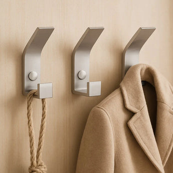 Trois crochets yessential.fr 10x Huso en acier inoxydable sont montés sur un mur beige : une corde épaisse pend au crochet de gauche, un manteau marron au crochet de droite et le crochet du milieu est vide.