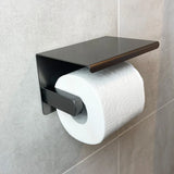 L'ensemble de toilettes Juano Gunmetal (sans perçage) de yessential.fr présente un rouleau de papier toilette sur un support élégant avec étagère, monté sur des carreaux gris clair - une mise à niveau moderne et élégante pour vos accessoires de salle de bain.