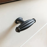 Un gros plan du bouton Alvaro Anthracite de yessential.fr, présentant un design nervuré en métal foncé de forme ovale sur une façade d'armoire ou de tiroir blanche.