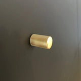 Un seul bouton Remo Gold Deluxe de yessential.fr, avec un design texturé cylindrique, est monté sur une surface lisse gris foncé.