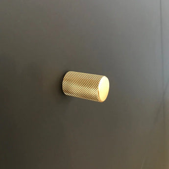 Un seul bouton Remo Gold Deluxe de yessential.fr, avec un design texturé cylindrique, est monté sur une surface lisse gris foncé.