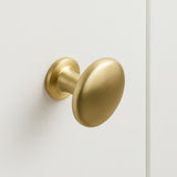 Le bouton d'armoire Pedro Gold avec sa finition ronde en or brossé, est monté sur une porte d'armoire blanche lisse et apporte une touche d'élégance à votre espace.