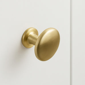 Le bouton d'armoire Pedro Gold avec sa finition ronde en or brossé, est monté sur une porte d'armoire blanche lisse et apporte une touche d'élégance à votre espace.