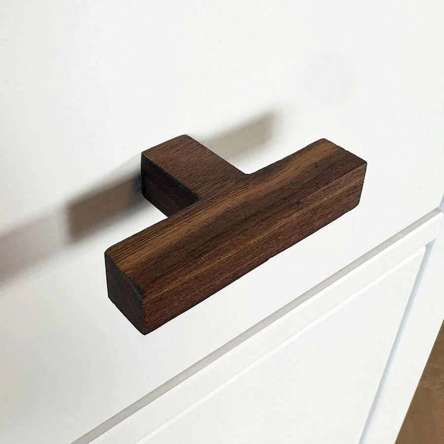 Le bouton Vigio Walnut de yessential.fr est installé sur une façade d'armoire blanche avec des détails de panneau simples.