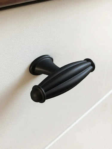 Un gros plan du bouton noir Alvaro de yessential.fr - une poignée d'armoire ovale noire avec des détails rainurés - montée sur une façade de tiroir blanche.