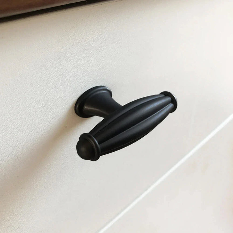 Un gros plan du bouton noir Alvaro de yessential.fr - une poignée d'armoire ovale noire avec des détails rainurés - montée sur une façade de tiroir blanche.