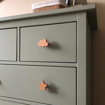 Une commode vert sauge avec les boutons Bambino Star de yessential.fr en forme de nuage et d'étoile. Il y a une boîte sur le dessus – idéale pour ajouter des boutons ludiques Bambino Star dans la chambre de votre enfant.