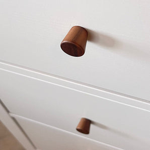 Gros plan de deux boutons en noyer Salgado de yessential.fr sur une armoire blanche, avec un bouton au point et l'autre légèrement flou en arrière-plan.