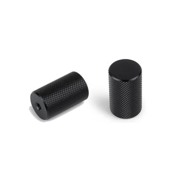 Deux poignées cylindriques Remo Black Deluxe de yessential.fr avec des surfaces métalliques texturées - l'une debout, l'autre couchée sur le côté révélant un trou à une extrémité - sur un fond blanc uni.