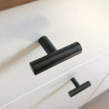 Gros plan d'un bouton Remo Black de yessential.fr sur un tiroir blanc, avec un autre bouton identique en dessous. Le coin souligne le design moderne et minimaliste de cette robinetterie élégante.