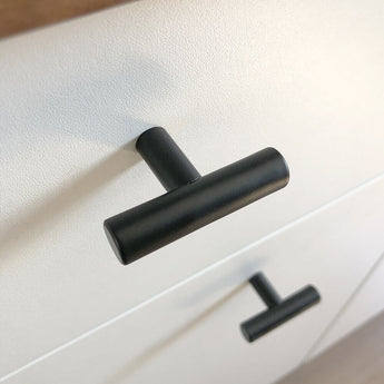 Gros plan d'un bouton Remo Black de yessential.fr sur un tiroir blanc, avec un autre bouton identique en dessous. Le coin souligne le design moderne et minimaliste de cette robinetterie élégante.