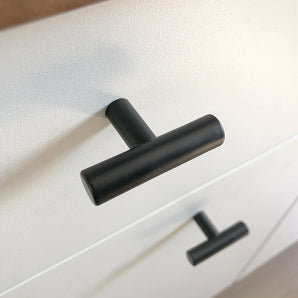 Gros plan d'un bouton Remo Black de yessential.fr sur un tiroir blanc, avec un autre bouton identique en dessous. Le coin souligne le design moderne et minimaliste de cette robinetterie élégante.