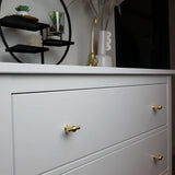 Une commode blanche avec 10 boutons Rando Gold de yessential.fr ajoute de l'élégance, surmontée de vases et d'une étagère ronde noire moderne contenant de petites plantes et des ornements.