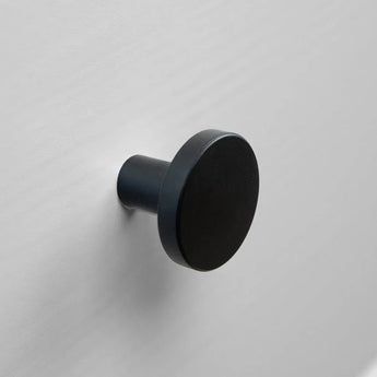 Le Marizo Black de yessential.fr est une patère murale ronde noire au fini mat, montée sur un mur gris clair. Son design minimaliste et sa face ronde et plate le rendent idéal comme bouton de meuble noir pour les intérieurs modernes.