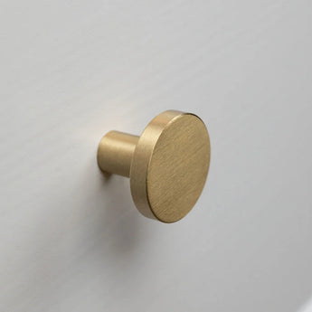 Monté sur une surface plane gris clair ou blanche, le bouton rond en laiton brossé Marizo Gold de yessential.fr apporte une sophistication élégante à n'importe quelle pièce.