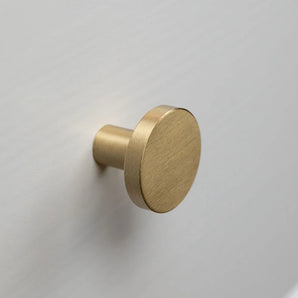 Monté sur une surface plane gris clair ou blanche, le bouton rond en laiton brossé Marizo Gold de yessential.fr apporte une sophistication élégante à n'importe quelle pièce.