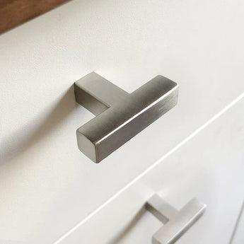 Un gros plan d'un bouton Vigio moderne en acier inoxydable de yessential.fr sur un tiroir blanc, avec un autre bouton similaire visible sur le tiroir ci-dessous.