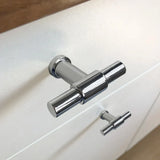 Gros plan du bouton 10x Cordero Chrome de yessential.fr monté sur un boîtier blanc : un bouton est net, l'autre flou. Un choix idéal pour les intérieurs modernes à la recherche de boutons de meubles chromés élégants.