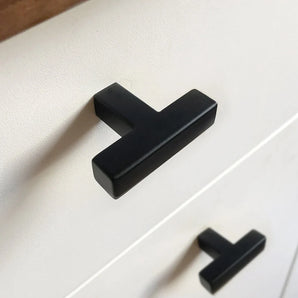 Gros plan d'une armoire blanche avec un bouton Vigio Black moderne noir mat de yessential.fr. Ces poignées en forme de T apportent une touche élégante lorsqu'elles sont montées horizontalement sur deux tiroirs.