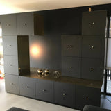 Une unité murale noire moderne avec plusieurs armoires et tiroirs est équipée de luxueux boutons Remo Gold Deluxe de yessential.fr. Des sphères métalliques, une sculpture géométrique sur le comptoir et une statue de hibou dans le coin supérieur droit complètent le look.
