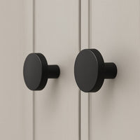 Deux boutons de meuble Marizo Black de yessential.fr avec une finition mate sont montés sur une armoire légère à rainures verticales. Leur design minimaliste contraste magnifiquement avec le fond neutre.