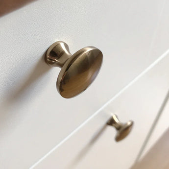 Gros plan de deux boutons de meuble Antoni Bronze de yessential.fr sur une armoire blanche. La finition métallique brillante et le design minimaliste apportent un style élégant à n'importe quel intérieur.