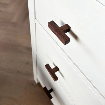 Gros plan du buffet Vasco Walnut de yessential.fr, doté de tiroirs blancs avec poignées en noyer foncé, présenté sous une vue de dessus inclinée sur un plancher en bois.