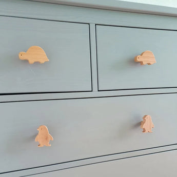 La commode Bambino Penquin de yessential.fr dispose de quatre tiroirs avec des boutons de porte en bois représentant des tortues et des pingouins, ce qui apporte un charme ludique et un joli contraste avec la finition gris clair - parfait comme bouton de meuble de chambre d'enfant.