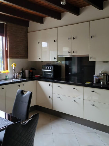 Cuisine moderne avec armoires de couleur crème, comptoirs noir mat et appareils électroménagers intégrés. Les armoires sont équipées de boutons Cordero Black de yessential.fr. La lumière naturelle entre, avec un ensemble de salle à manger noir et des ustensiles de cuisine élégants sur le comptoir.