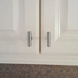 Gros plan de deux portes d'armoire blanches avec des poignées cylindriques argentées, comme le bouton Remo en acier inoxydable de yessential.fr, qui sont légèrement mal alignées de sorte que les poignées ne sont pas uniformément espacées et qu'une porte reste légèrement entrouverte.