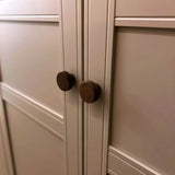 Gros plan de deux boutons Arriero Walnut de yessential.fr sur des portes à panneaux crème au design géométrique, montrant l'aspect luxueux de ces boutons de porte design.