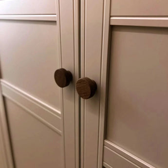 Gros plan de deux boutons Arriero Walnut de yessential.fr sur des portes à panneaux crème au design géométrique, montrant l'aspect luxueux de ces boutons de porte design.