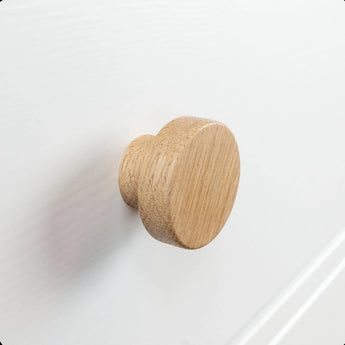 Un gros plan du bouton Arriero Oak de yessential.fr, fixé à un tiroir blanc, met en valeur le grain naturel du bois et la finition lisse, ajoutant une touche de style campagnard.