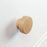 Un gros plan du bouton Arriero Oak de yessential.fr, fixé à un tiroir blanc, met en valeur le grain naturel du bois et la finition lisse, ajoutant une touche de style campagnard.