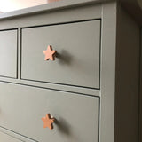 Gros plan d'une commode grise avec deux tiroirs, chacun équipé de boutons en bois clair yessential.fr Bambino Star. Cette commode simple et moderne est idéale pour ajouter du charme à une chambre de bébé avec ces boutons de chambre de bébé uniques.