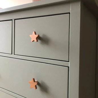 Gros plan d'une commode grise avec deux tiroirs, chacun équipé de boutons en bois clair yessential.fr Bambino Star. Cette commode simple et moderne est idéale pour ajouter du charme à une chambre de bébé avec ces boutons de chambre de bébé uniques.