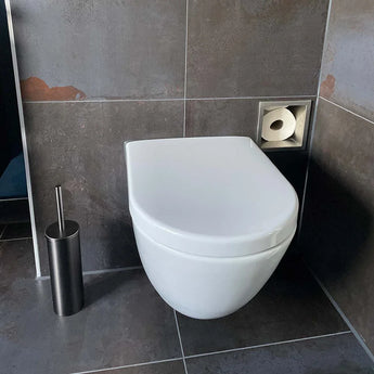 Dans la salle de bain carrelée sombre, un WC suspendu blanc avec réservoir caché, associé à l'ensemble WC Tapio Gunmetal (sans perçage) de yessential.fr - avec un porte-balai en acier inoxydable et un porte-papier encastré, se démarque.