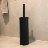L'ensemble de toilette Juano Black (sans perçage) de yessential.fr, composé d'une brosse de toilette noire avec un support cylindrique assorti, est posé sur un carrelage de couleur claire à proximité d'une serviette beige accrochée au mur.