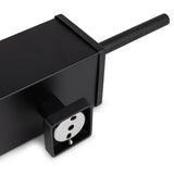 Gros plan sur la multiprise Alessino Black de yessential.fr, avec une prise européenne et un cordon noir, placée à côté d'une brosse WC noire mate pour un style de salle de bain épuré et moderne.