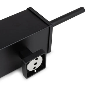 Gros plan sur la multiprise Alessino Black de yessential.fr, avec une prise européenne et un cordon noir, placée à côté d'une brosse WC noire mate pour un style de salle de bain épuré et moderne.