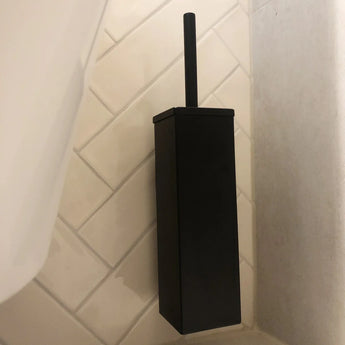 L'ensemble de toilettes Venzo Black de yessential.fr, avec un support rectangulaire moderne et un design carré, est placé sur un sol carrelé en diagonale blanche dans un coin de salle de bain.
