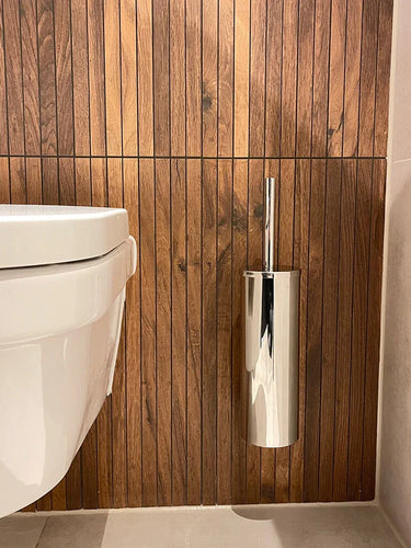 Des toilettes suspendues blanches modernes sont associées à l'ensemble de toilettes Romano Chrome de yessential.fr, contre un mur vertical avec des panneaux en bois et un sol carrelé de couleur claire.